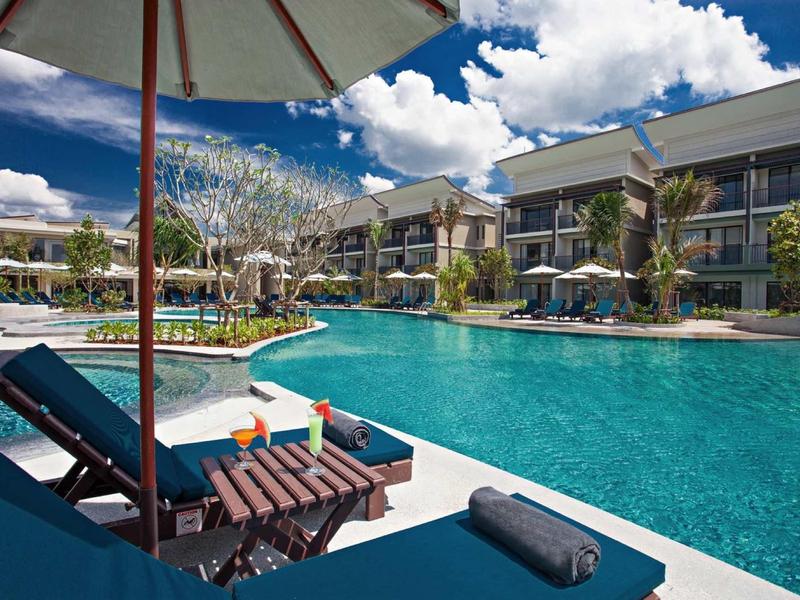 Modern buitenzwembad met ligstoelen en parasols bij een hotelresort bij zonnig weer.