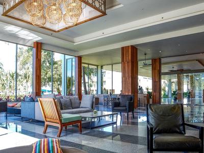 Lichte hotellounge met grote ramen, moderne fauteuils en decoratief tapijt.