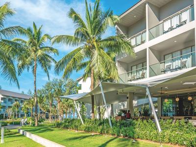 Modern hotelcomplex met buitenzwembad, loungegedeelte en palmbomen onder een blauwe lucht.