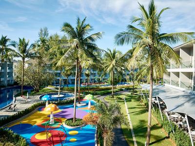 Hotel tuin met palmbomen, kleurrijke speeltuin voor kinderen en ligstoelen onder blauwe lucht.