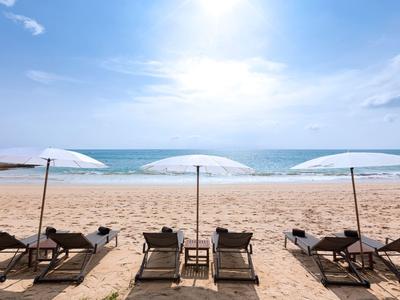 Tři slunečníky a lehátka na písečné pláži s výhledem na oceán za jasné oblohy.