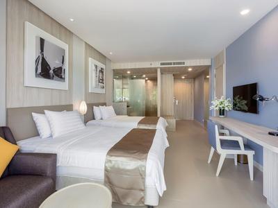 Lichte hotelkamer met twee bedden, bureau, tv en open badkamer.