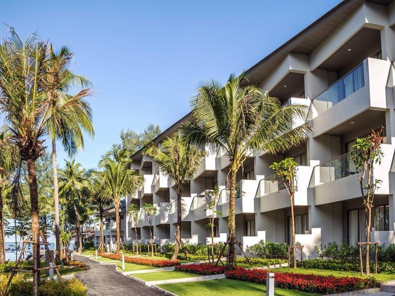 Modern hotelcomplex met balkons, omringd door palmbomen en verzorgd groen bij heldere lucht.