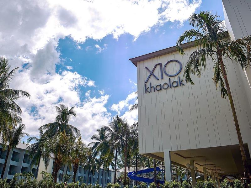 Modern hotelcomplex met palmbomen onder een bewolkte lucht.