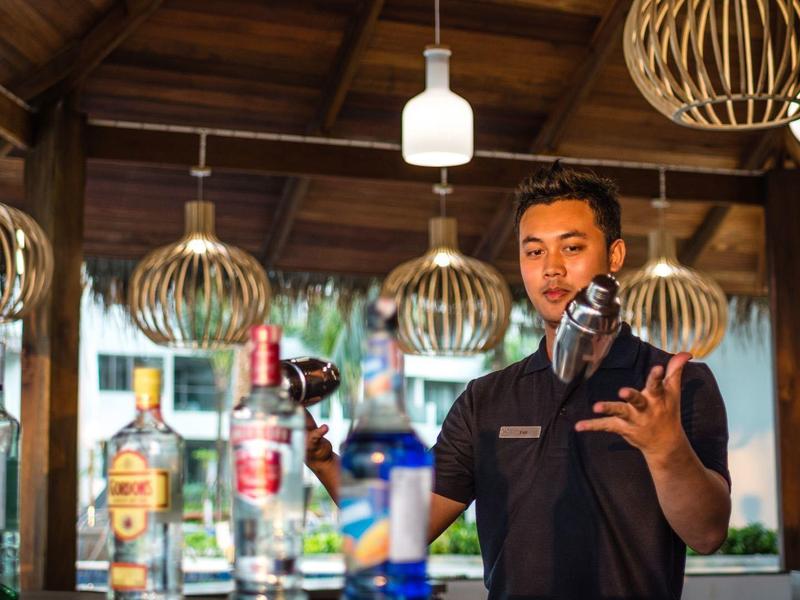 Barman schenkt fles over glas in stijlvolle bar met houten plafond en moderne lampen.