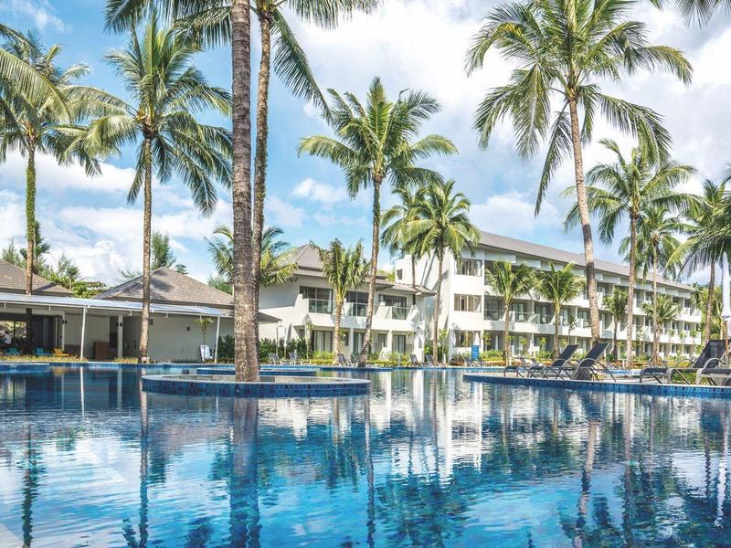 Hotelcomplex met groot zwembad, omringd door palmbomen en moderne gebouwen.