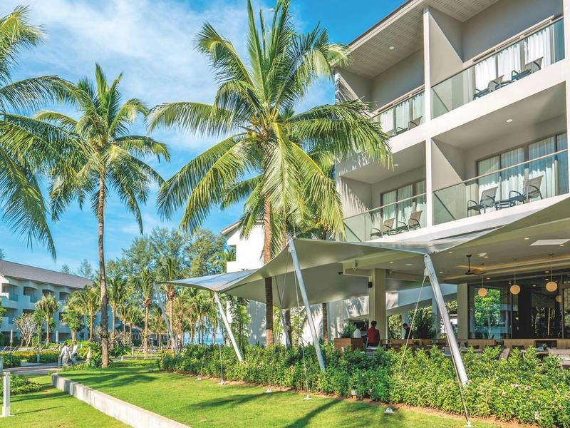 Modern hotelcomplex met buitenzwembad, loungegedeelte en palmbomen onder een blauwe lucht.