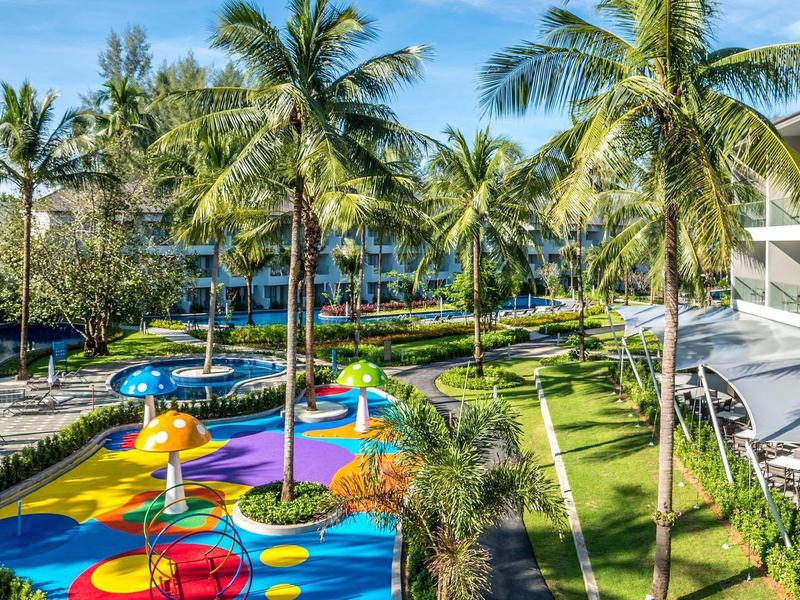 Kleurrijke waterspeeltuin omringd door palmbomen in tropisch resort met hotels.