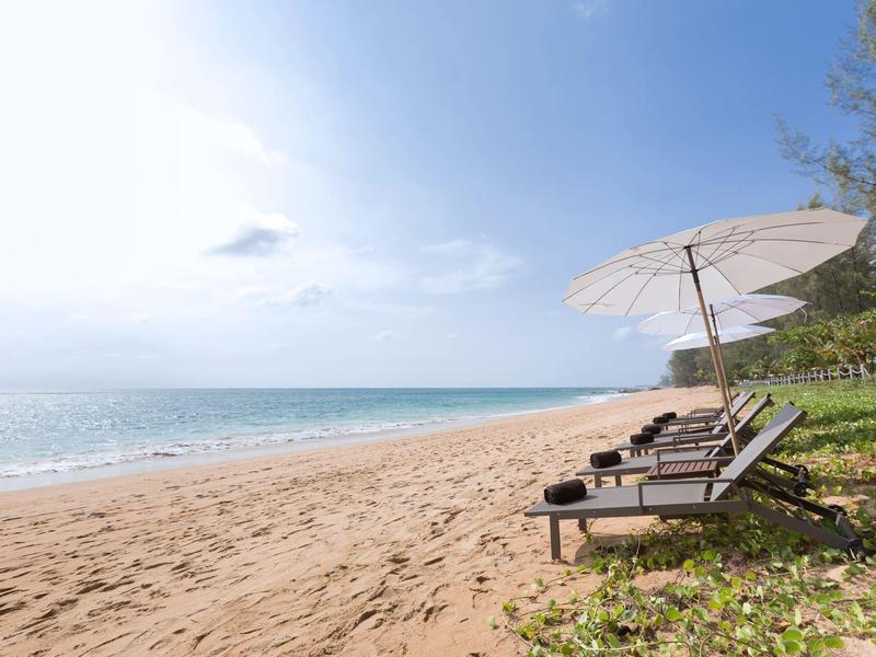 Lege ligstoelen met parasol op rustig zandstrand en blauwe lucht.