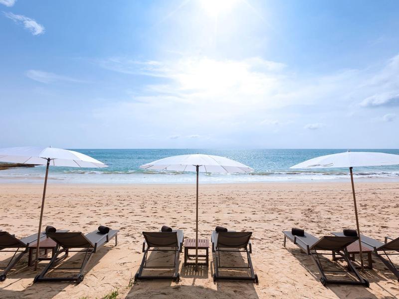 Drie ligstoelen met witte parasols op zandstrand bij de rustige zee.