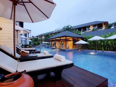 Zwembadgebied met ligstoelen en parasols voor hotelgebouwen bij bewolkte lucht.