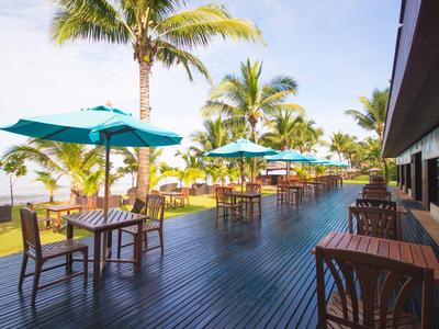 Groot houten terras met tafels, stoelen, blauwe parasols, palmbomen en zeezicht