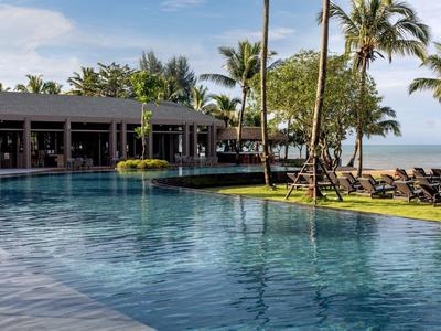 Groot zwembad met uitzicht op de zee, omgeven door palmbomen en ligstoelen.