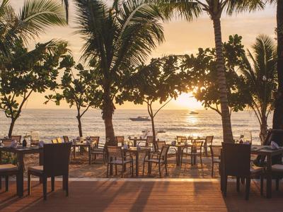 Strefa do siedzenia ze stolikami i krzesłami na plaży o zachodzie słońca z palmami.