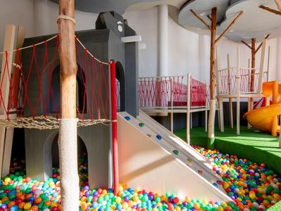 Overdekte speeltuin met glijbaan, klimstructuur en kleurrijk ballenbad in een hotel.