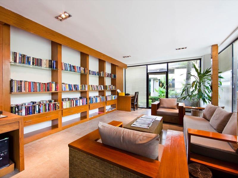 Lichte hotelkamer met boekenplanken, comfortabele fauteuils en groot raam met uitzicht op groen.