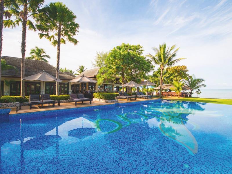 Groot zwembad met ligbedden en palmbomen op een zonnige dag bij het hotelresort aan zee.