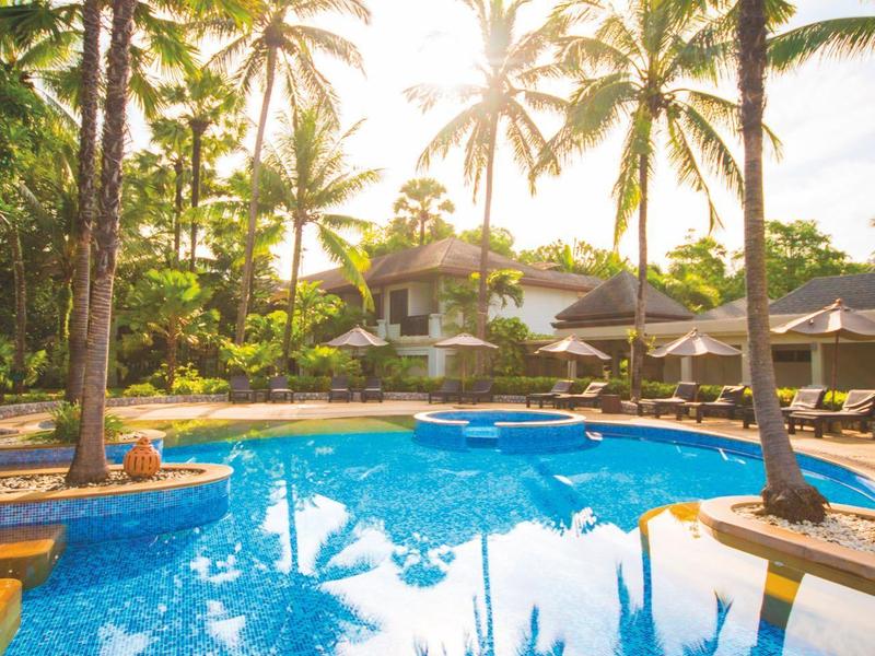 Zwembad met helder water en hoge palmbomen in een tropisch resort bij zonsondergang.