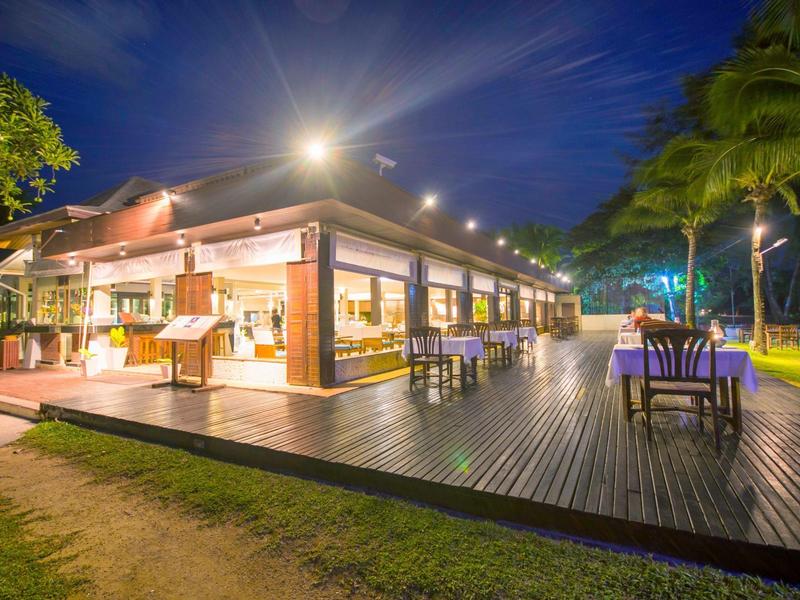 Modern verlicht restaurant met buitenzitplaatsen en houten terras bij nacht.