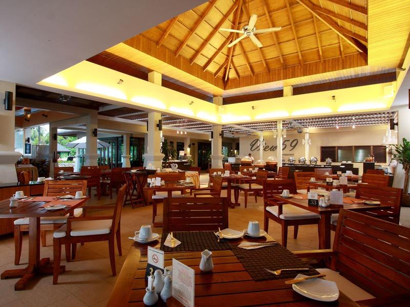 Open restaurant met houten meubels en hoog plafond in een tropisch hotel.