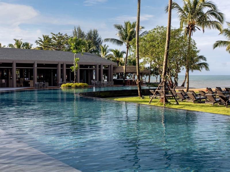 Groot zwembad met uitzicht op de zee, omgeven door palmbomen en ligstoelen.