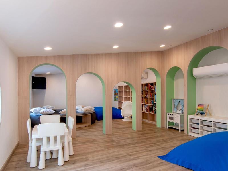 Speel- en slaapgedeelte voor kinderen met houten vloeren, kleurrijk meubilair en afgeronde deuropeningen.