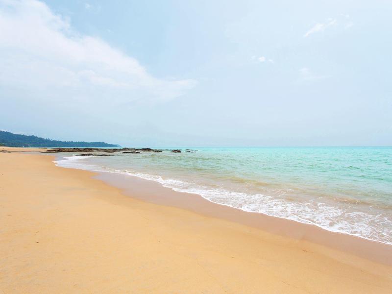 Wide empty sandy beach with gentle waves and blue sky.