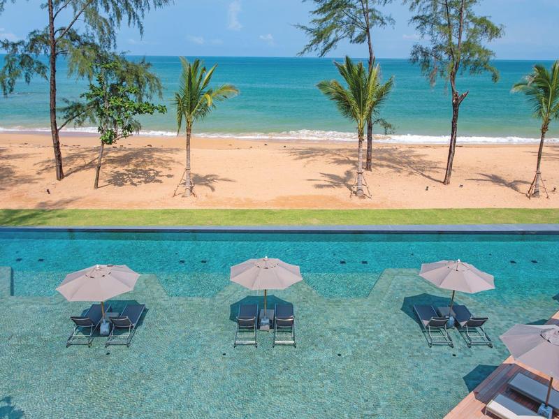 View of pool with lounge chairs and umbrellas at the beach by the sea.