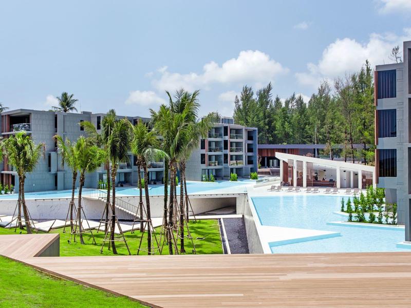 Modern resort with pools, palm trees, and multi-story buildings under a blue sky.