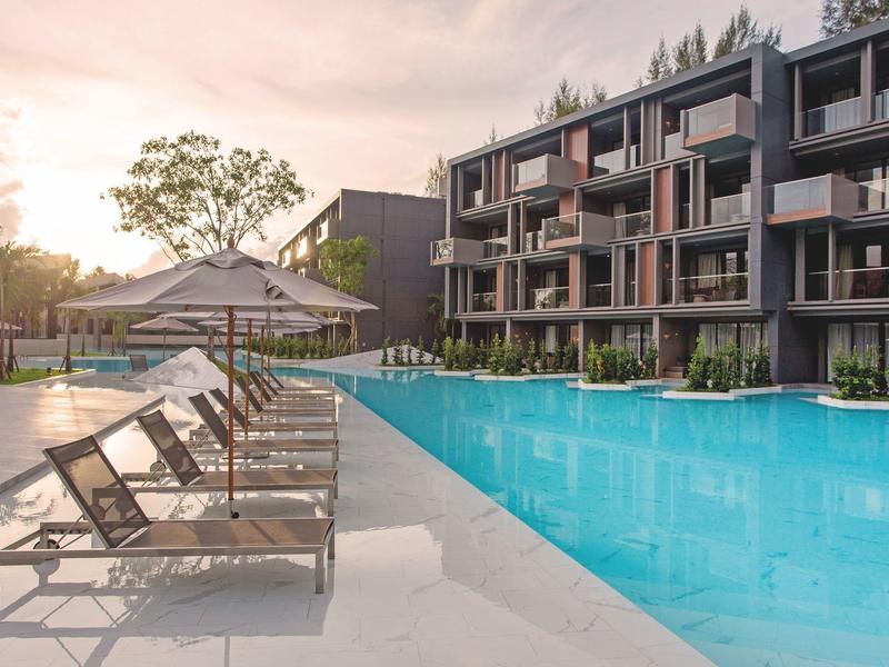 Modern hotel pool with lounge chairs and multi-story building at sunset.