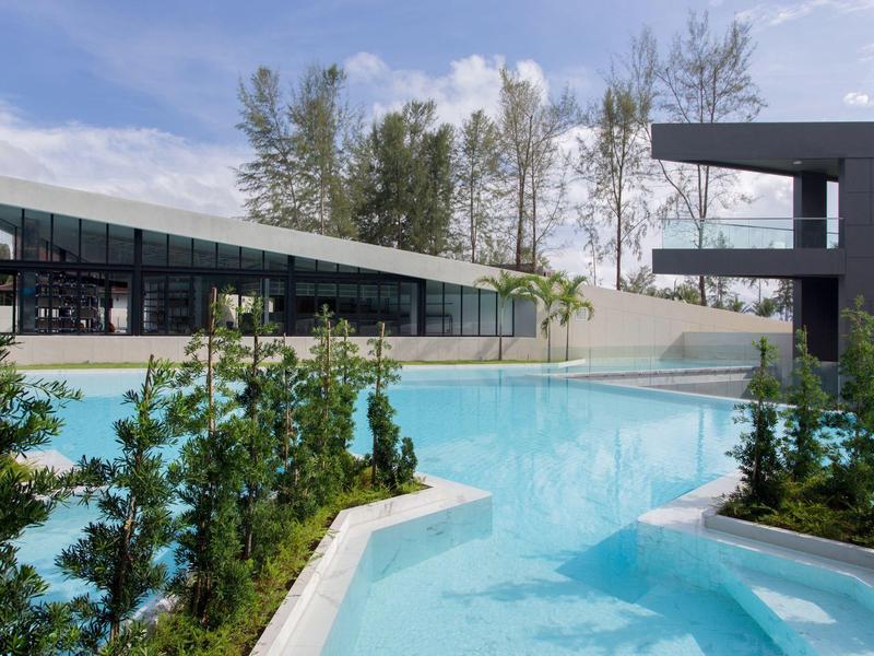 Modern hotel pool with clear water surrounded by trees under a blue sky.