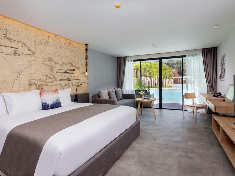 Modern hotel room with large bed, sofa, flat-screen TV and balcony overlooking garden