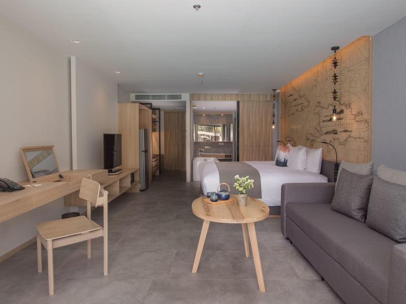 Modern hotel room with sofa, desk, chairs, and large bed in a calm setting.