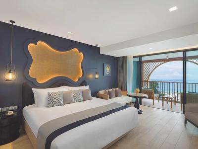 Habitación de hotel moderna con cama grande, iluminación de pared elegante y balcón con vista al mar.