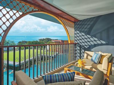Balcón con muebles y vistas al mar, piscina y césped en un hotel tropical.