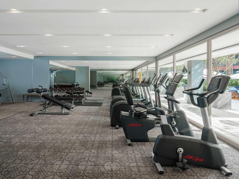 Gimnasio moderno con varias cintas de correr, pesas y grandes ventanas que dejan entrar mucha luz natural.