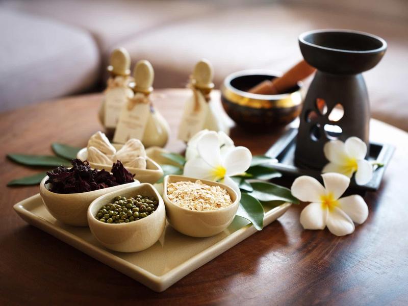 Aceite de masaje, especias y flores dispuestas en una bandeja para un tratamiento relajante.