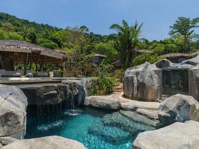Piscina natural con rocas, cascada y vegetación tropical alrededor.