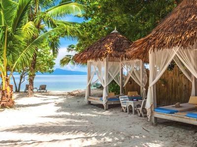 Spiaggia con palme, due letti a baldacchino con tende e vista mare.