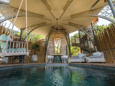 Area piscina coperta con altalena e mobili da lounge in un ambiente tropicale.