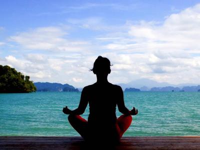 Persona sentada con piernas cruzadas en una plataforma de madera con vista al mar y cielo nublado.