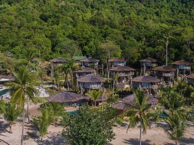 Bungalow con tetti di paglia al margine della foresta vicino a una spiaggia sabbiosa con palme