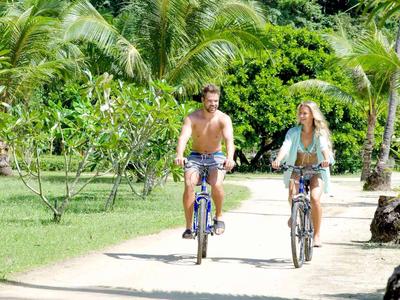 Una coppia va in bicicletta su un sentiero soleggiato fiancheggiato da palme.