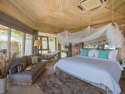 Camera d'hotel accogliente con letto grande, zanzariera e area salotto con divano e amaca.