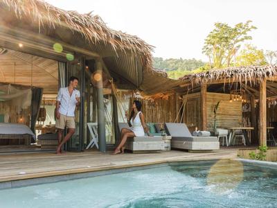 Pareja disfrutando de un momento relajante en la terraza de un alojamiento tropical con piscina.