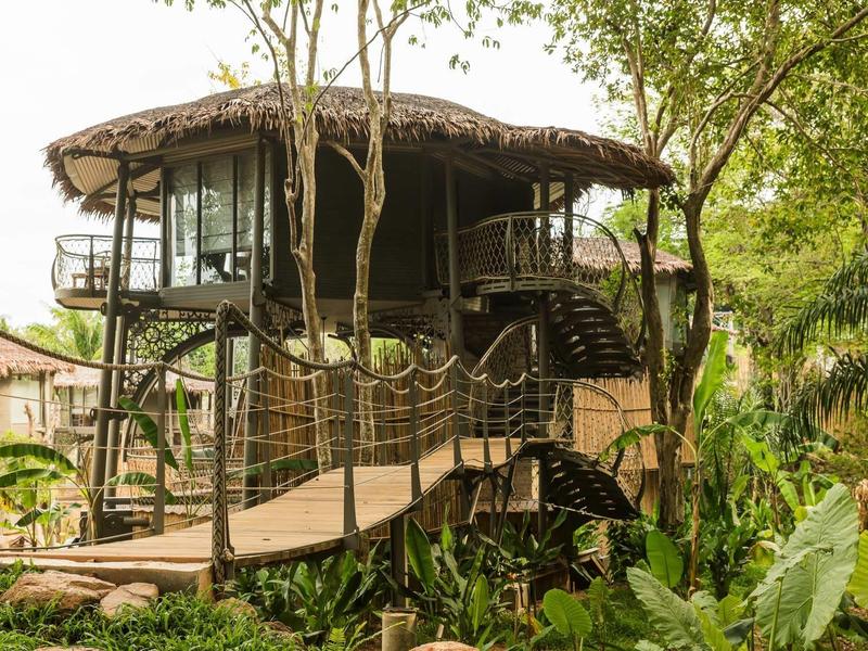 Una casa sull'albero con un ponte di legno circondata da una giungla verde e fitta.
