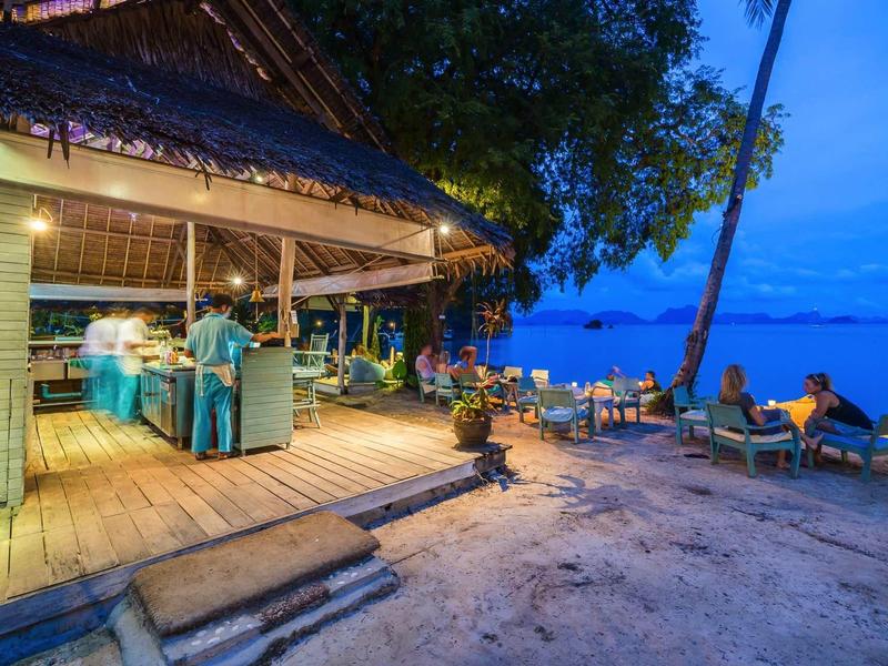 Bar sulla spiaggia al crepuscolo con posti a sedere e vista sul mare.