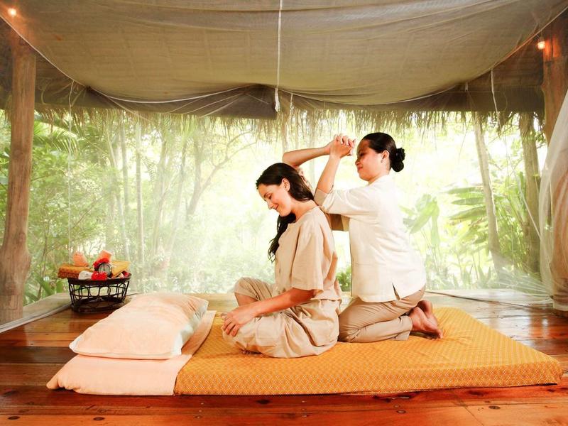 Una donna riceve un massaggio tradizionale thailandese in uno spazio aperto circondato dalla natura.