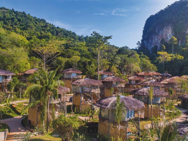 Panorama di un resort con bungalow in un ambiente tropicale davanti a montagne boschive.