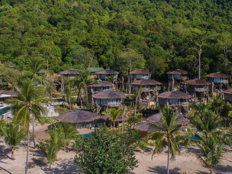 Bungalow con tetti di paglia al margine della foresta vicino a una spiaggia sabbiosa con palme
